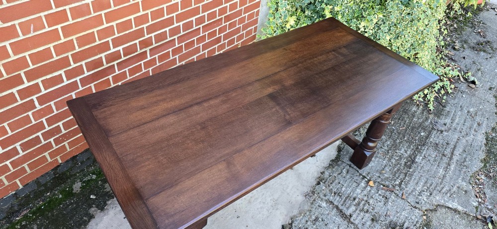 A solid dark oak refectory dining table with a plank top, stout turned legs, and an H-stretcher base. View V