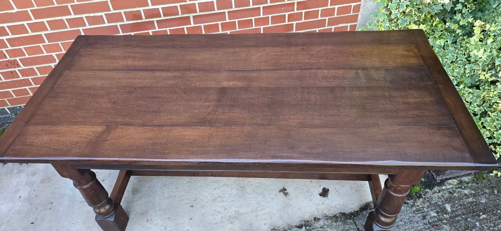 A solid dark oak refectory dining table with a plank top, stout turned legs, and an H-stretcher base. View XI