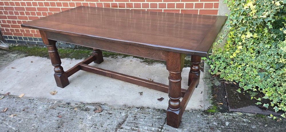 A solid dark oak refectory dining table with a plank top, stout turned legs, and an H-stretcher base. View XII