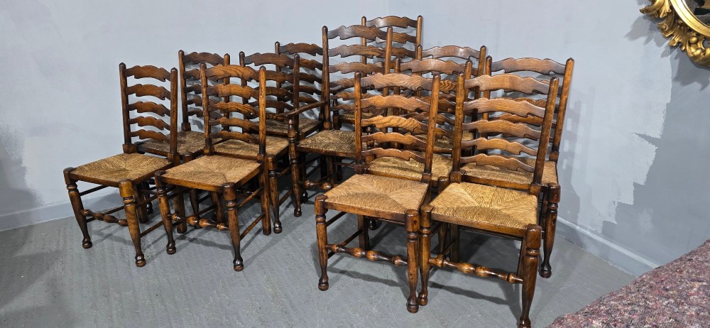 A set of twelve oak dining chairs featuring shaped ladder back slats, natural rush seats, and turned front legs. View VII