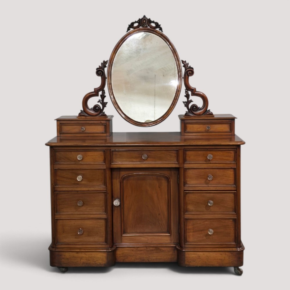 A Victorian mahogany dressing table featuring a central oval swivelling mirror, carved scroll supports, small upper trinket drawers, and twin drawer pedestals flanking a central cupboard.