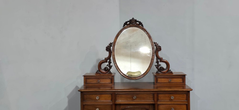 A Victorian mahogany dressing table featuring a central oval swivelling mirror, carved scroll supports, small upper trinket drawers, and twin drawer pedestals flanking a central cupboard. View III