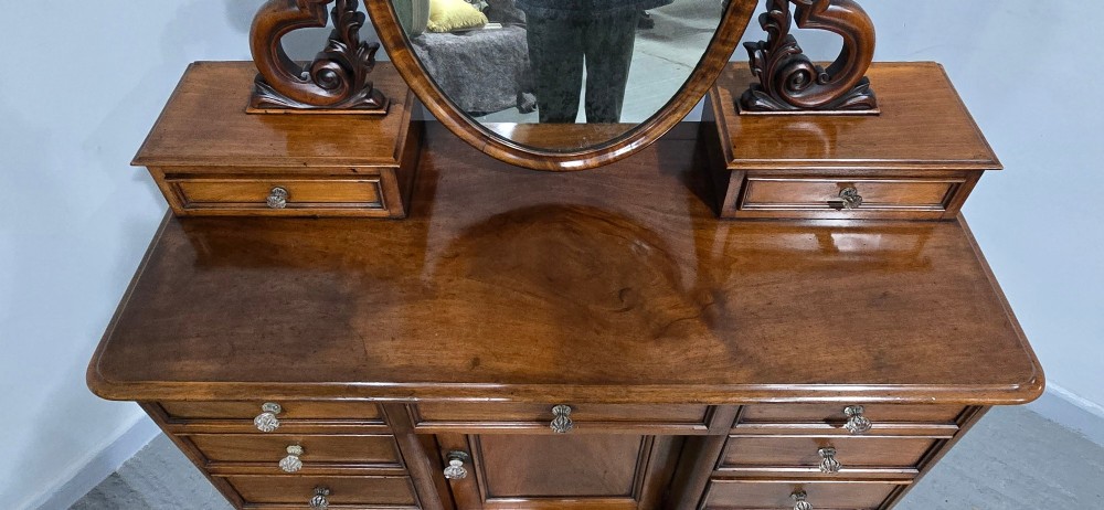 A Victorian mahogany dressing table featuring a central oval swivelling mirror, carved scroll supports, small upper trinket drawers, and twin drawer pedestals flanking a central cupboard. View IV