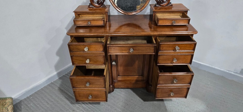 A Victorian mahogany dressing table featuring a central oval swivelling mirror, carved scroll supports, small upper trinket drawers, and twin drawer pedestals flanking a central cupboard. View IX