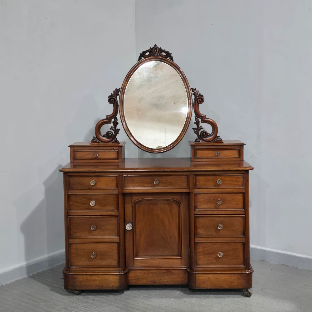 A Victorian mahogany dressing table featuring a central oval swivelling mirror, carved scroll supports, small upper trinket drawers, and twin drawer pedestals flanking a central cupboard. View XIII