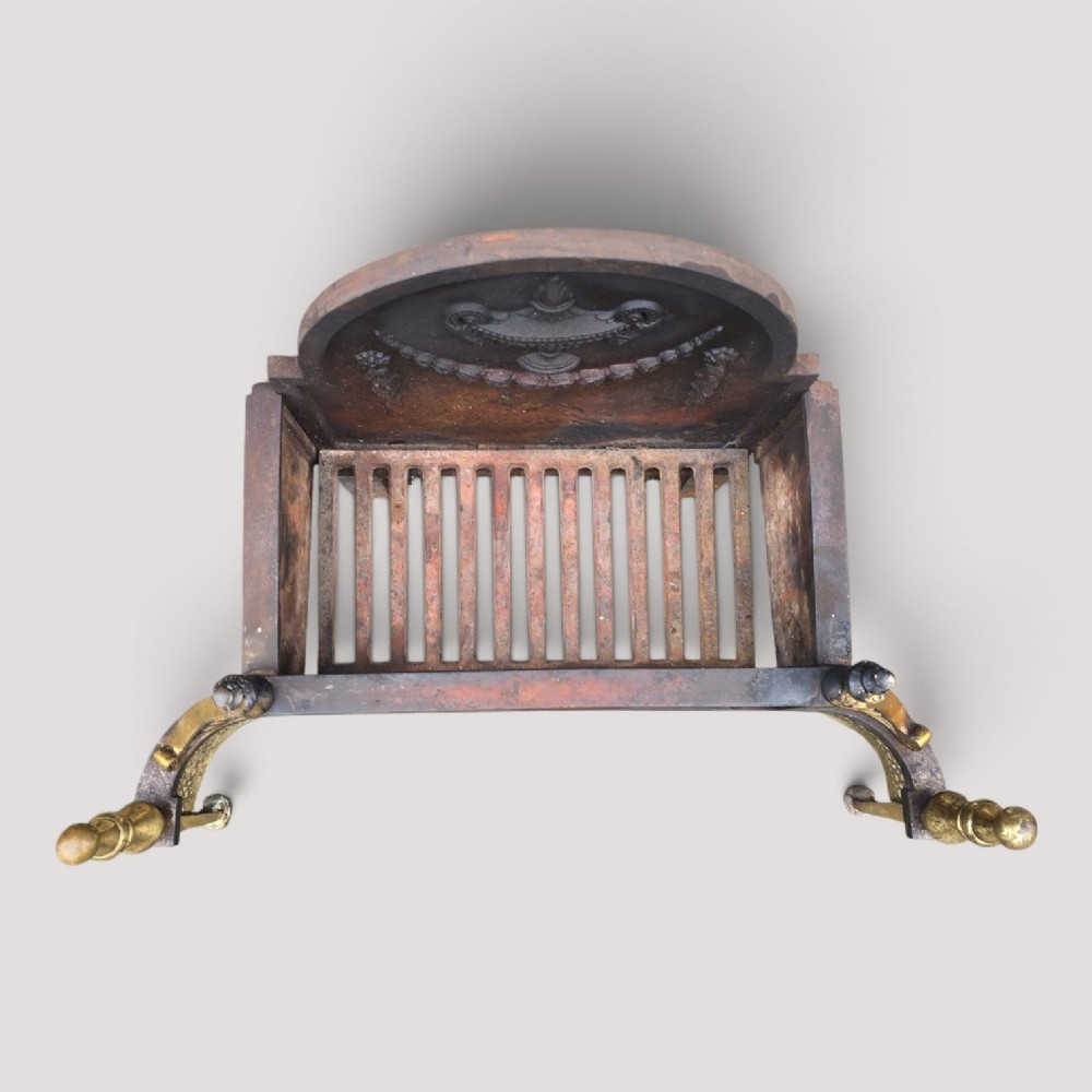 An Adam style fireplace dog grate crafted from cast iron and brass, featuring a serpentine pierced apron, urn finials, and a relief urn backplate. View II