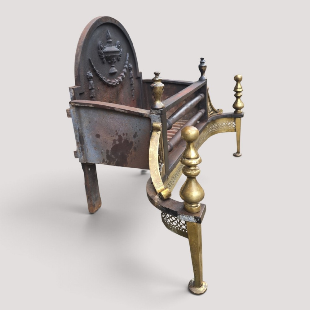 An Adam style fireplace dog grate crafted from cast iron and brass, featuring a serpentine pierced apron, urn finials, and a relief urn backplate. View IV