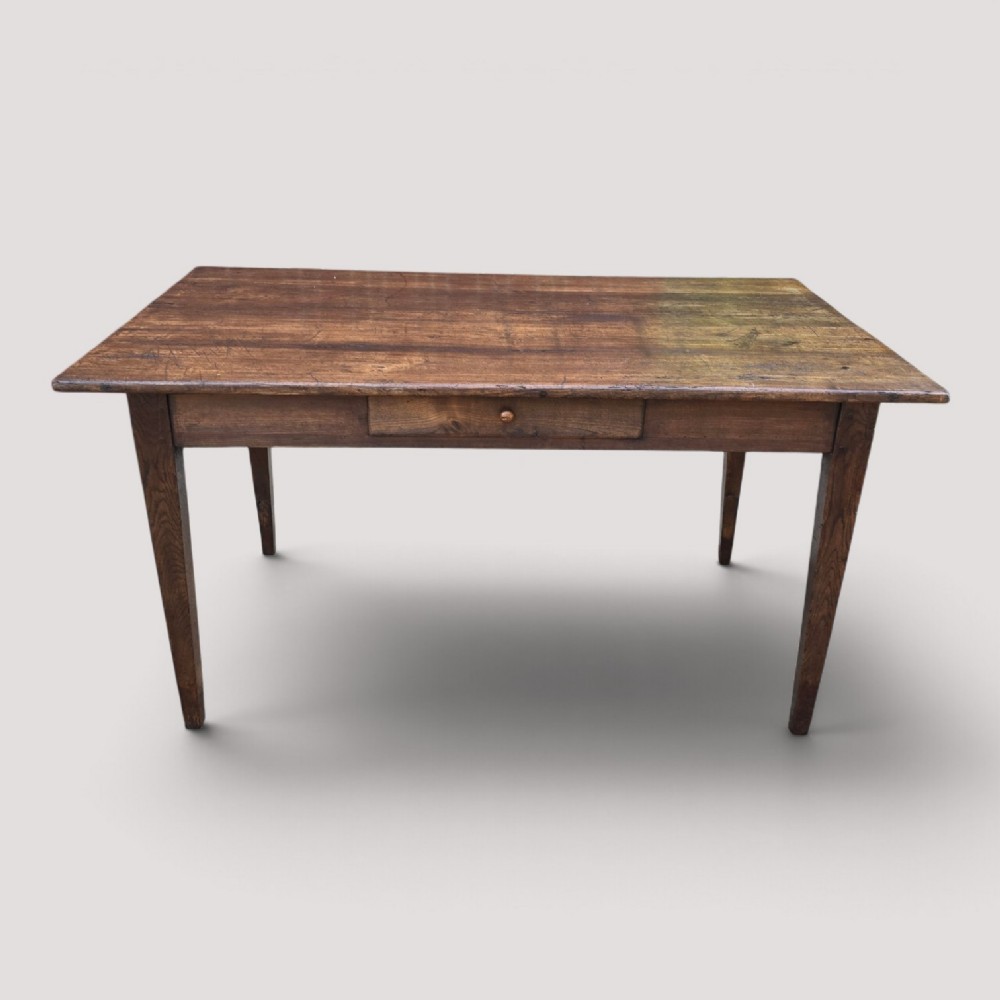 A rectangular rustic oak dining table featuring a frieze drawer with a wooden knob and four square tapered legs.
