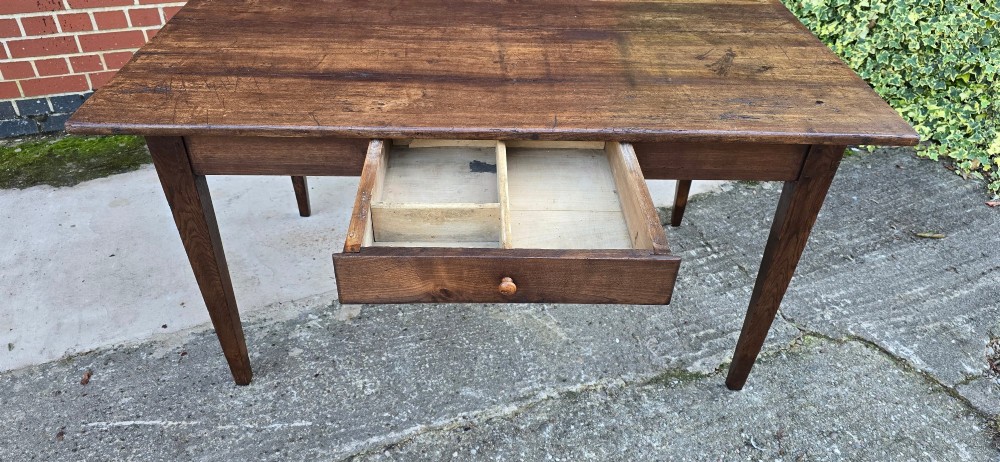A rectangular rustic oak dining table featuring a frieze drawer with a wooden knob and four square tapered legs. View VII