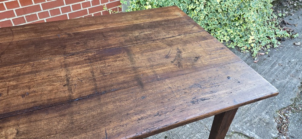 A rectangular rustic oak dining table featuring a frieze drawer with a wooden knob and four square tapered legs. View X