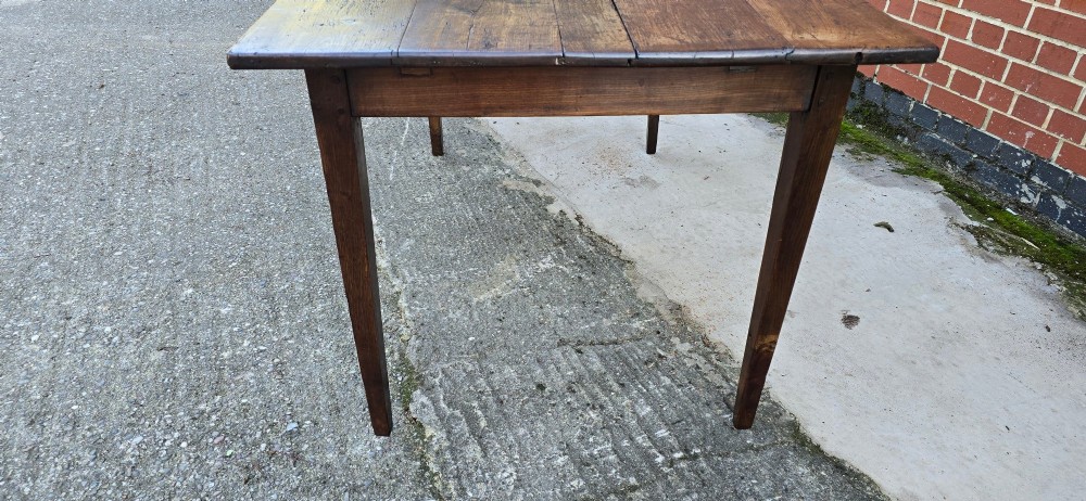 A rectangular rustic oak dining table featuring a frieze drawer with a wooden knob and four square tapered legs. View XII