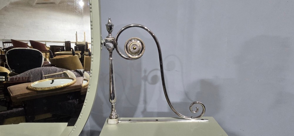 A sage green painted dressing table featuring an integrated central shield mirror, side trinket drawers, metal scroll sconces, and tapered legs. View XIII