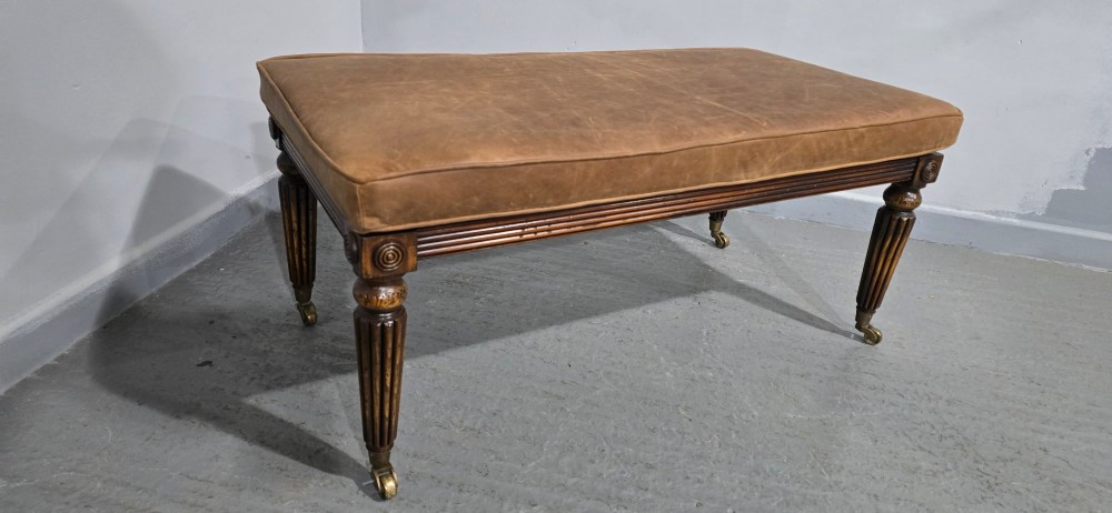 A rectangular Regency bench featuring tan leather upholstery, a reeded dark wood frame, tapered carved legs, and brass castors. View VI