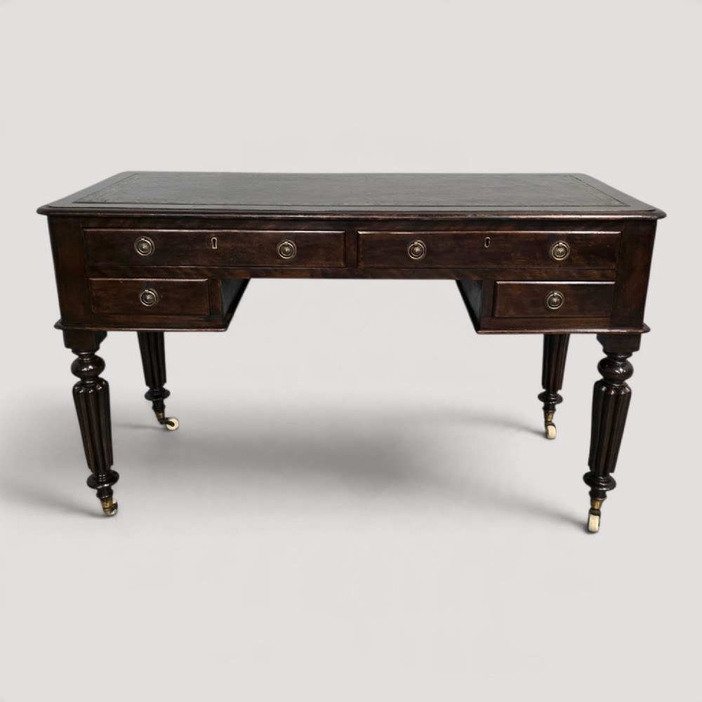 A Victorian dark mahogany writing desk featuring a green leather inset top, four drawers with circular brass ring handles, turned fluted legs, and brass castors.