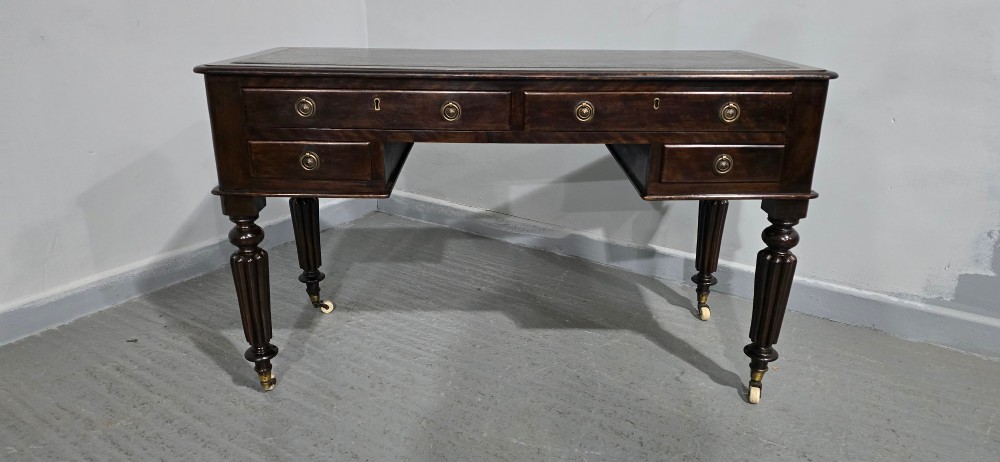A Victorian dark mahogany writing desk featuring a green leather inset top, four drawers with circular brass ring handles, turned fluted legs, and brass castors. View II