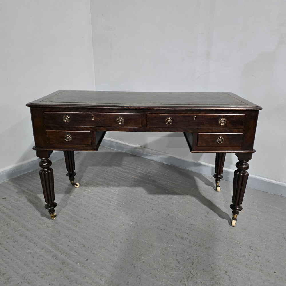 A Victorian dark mahogany writing desk featuring a green leather inset top, four drawers with circular brass ring handles, turned fluted legs, and brass castors. View III