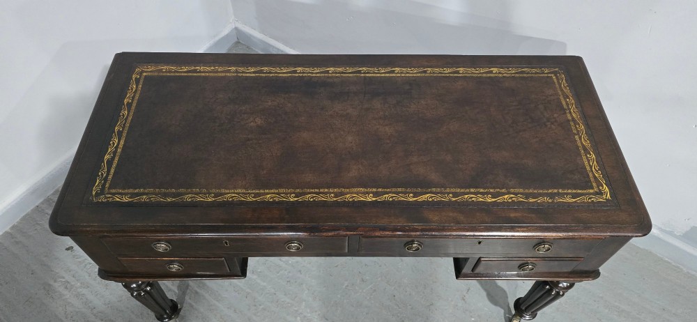 A Victorian dark mahogany writing desk featuring a green leather inset top, four drawers with circular brass ring handles, turned fluted legs, and brass castors. View IV