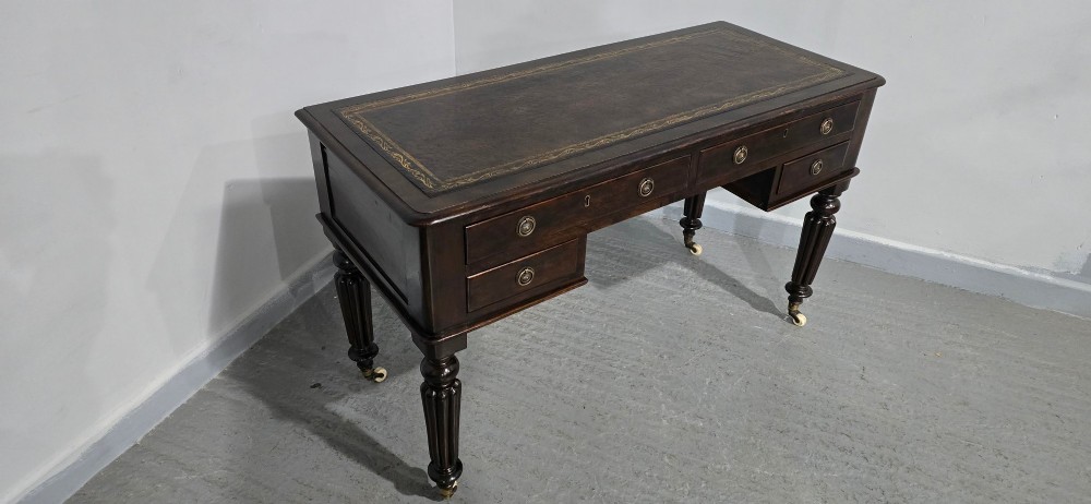 A Victorian dark mahogany writing desk featuring a green leather inset top, four drawers with circular brass ring handles, turned fluted legs, and brass castors. View VII