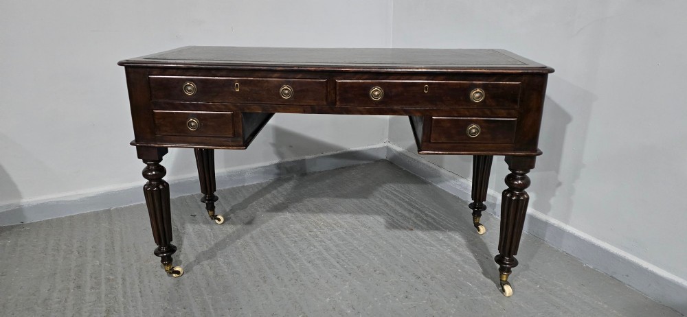 A Victorian dark mahogany writing desk featuring a green leather inset top, four drawers with circular brass ring handles, turned fluted legs, and brass castors. View IX