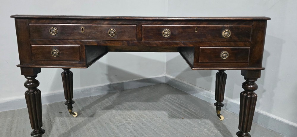 A Victorian dark mahogany writing desk featuring a green leather inset top, four drawers with circular brass ring handles, turned fluted legs, and brass castors. View XI