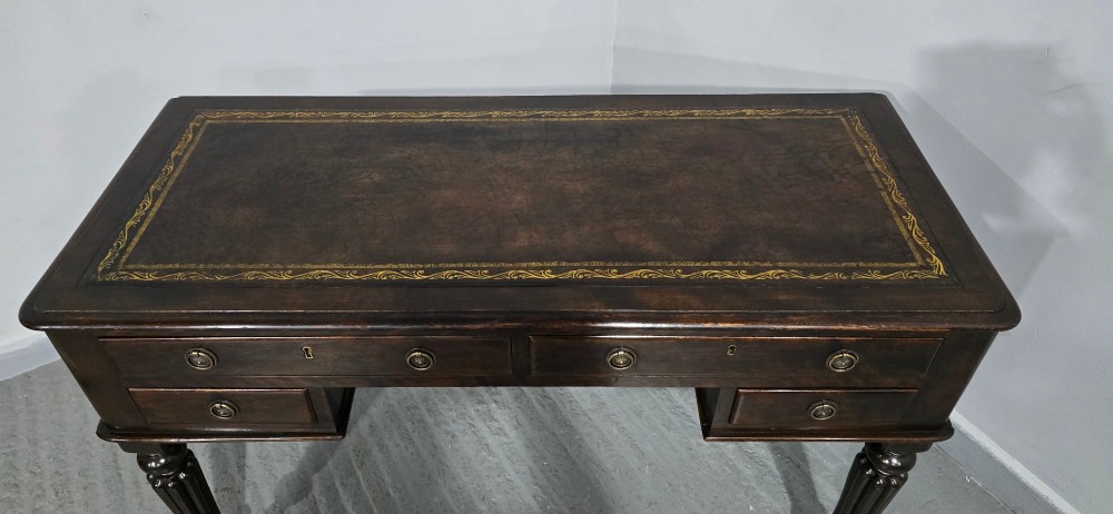 A Victorian dark mahogany writing desk featuring a green leather inset top, four drawers with circular brass ring handles, turned fluted legs, and brass castors. View XII