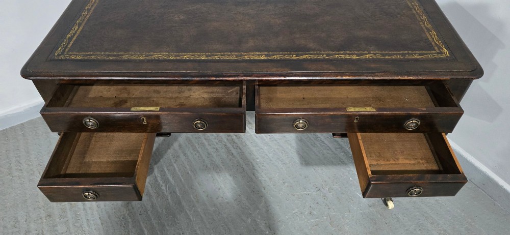 A Victorian dark mahogany writing desk featuring a green leather inset top, four drawers with circular brass ring handles, turned fluted legs, and brass castors. View XIII