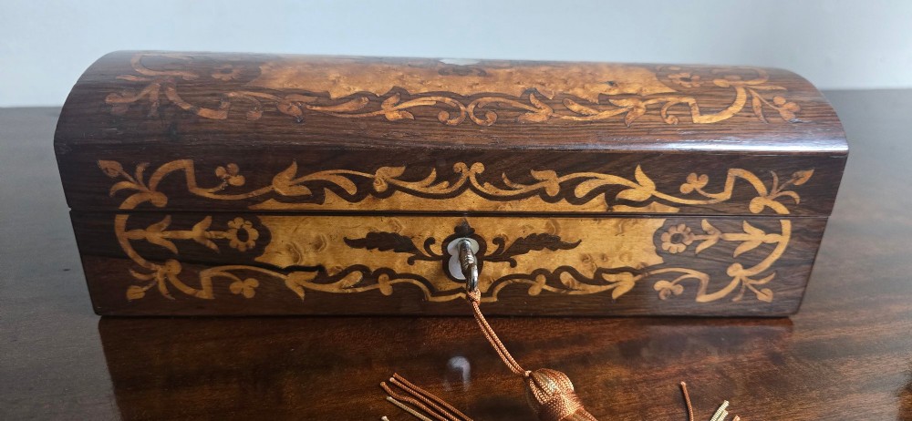 An antique dark wood rectangular glove box featuring foliate marquetry inlay, a curved lid, a key with a silk tassel, and a mother-of-pearl escutcheon. View II