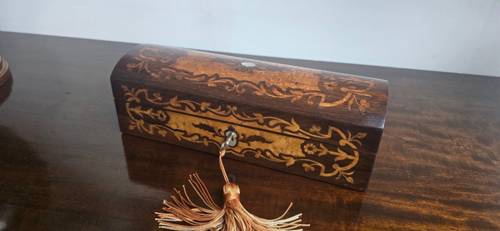An antique dark wood rectangular glove box featuring foliate marquetry inlay, a curved lid, a key with a silk tassel, and a mother-of-pearl escutcheon. View III