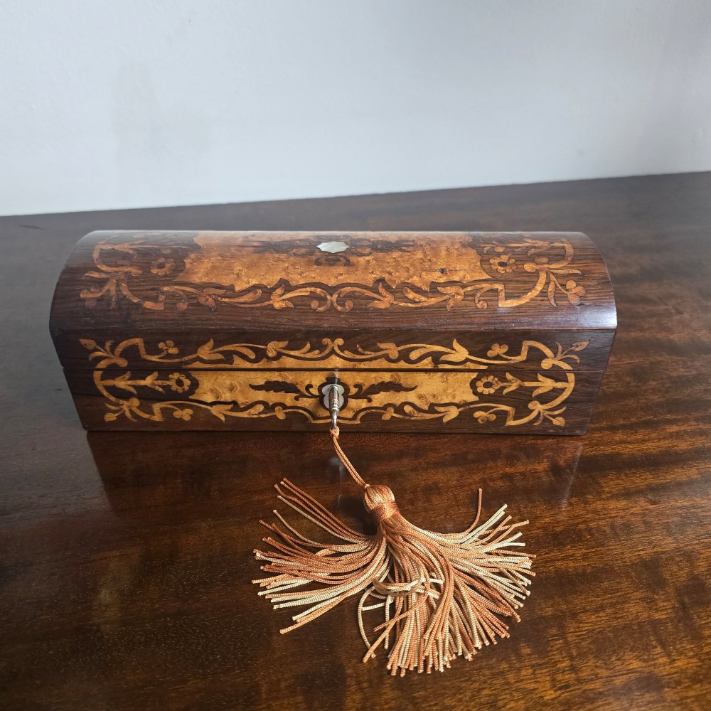 An antique dark wood rectangular glove box featuring foliate marquetry inlay, a curved lid, a key with a silk tassel, and a mother-of-pearl escutcheon. View V