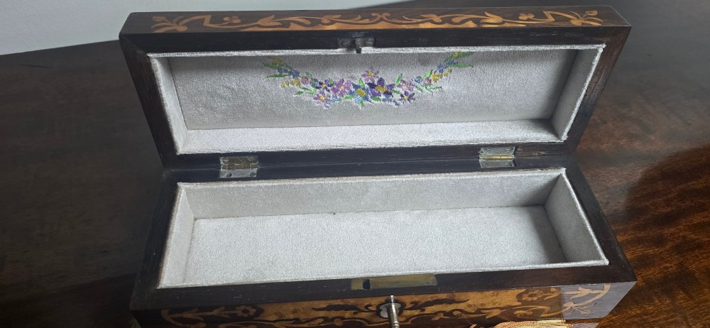 An antique dark wood rectangular glove box featuring foliate marquetry inlay, a curved lid, a key with a silk tassel, and a mother-of-pearl escutcheon. View IX