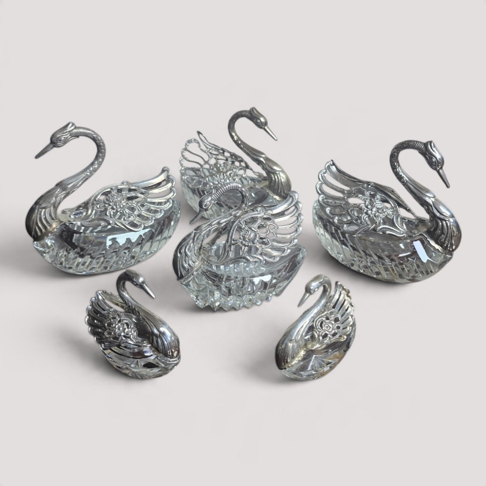 A group of cut glass open salt cellars shaped like swans with silver heads and detailed pierced silver wings.