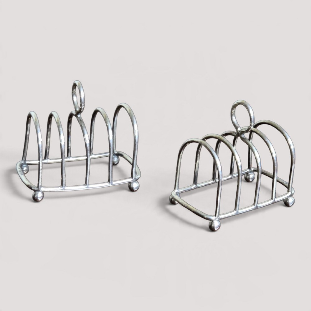 A pair of Edwardian sterling silver toast racks featuring arched wire dividers, central loop handles, and small ball feet.