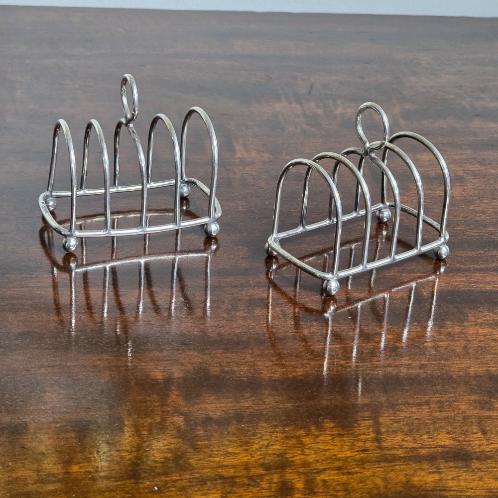 A pair of Edwardian sterling silver toast racks featuring arched wire dividers, central loop handles, and small ball feet. View II