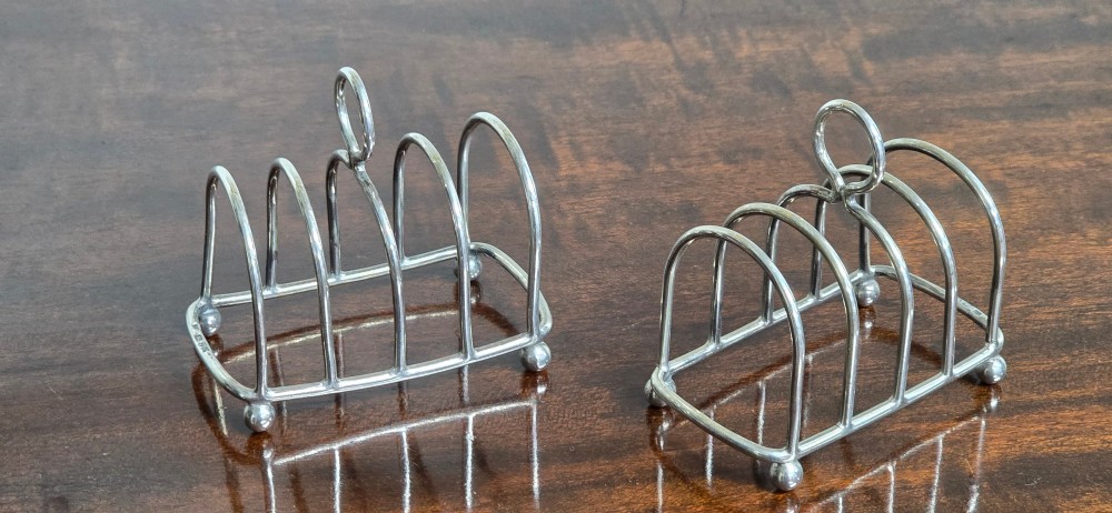 A pair of Edwardian sterling silver toast racks featuring arched wire dividers, central loop handles, and small ball feet. View III