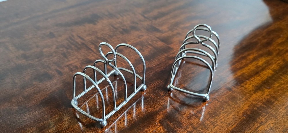 A pair of Edwardian sterling silver toast racks featuring arched wire dividers, central loop handles, and small ball feet. View IV