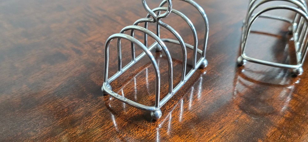 A pair of Edwardian sterling silver toast racks featuring arched wire dividers, central loop handles, and small ball feet. View V