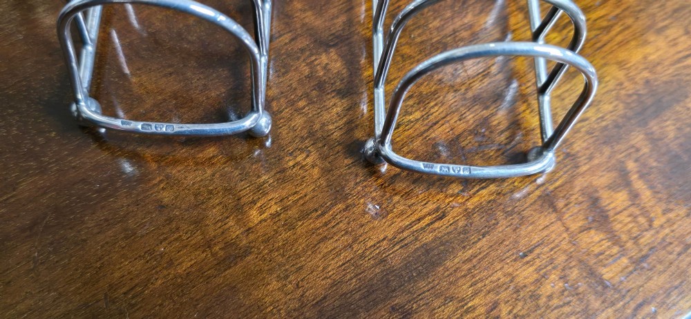 A pair of Edwardian sterling silver toast racks featuring arched wire dividers, central loop handles, and small ball feet. View VI