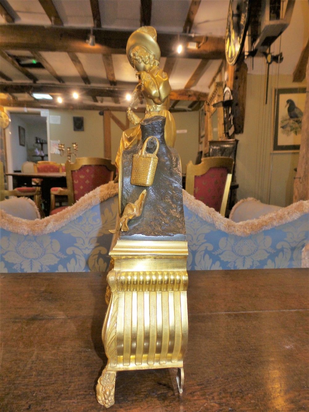 A mid-19th-century French gilt bronze and patinated bronze mantel clock featuring a seated female figure holding a fan atop an ornate sculpted base. View V