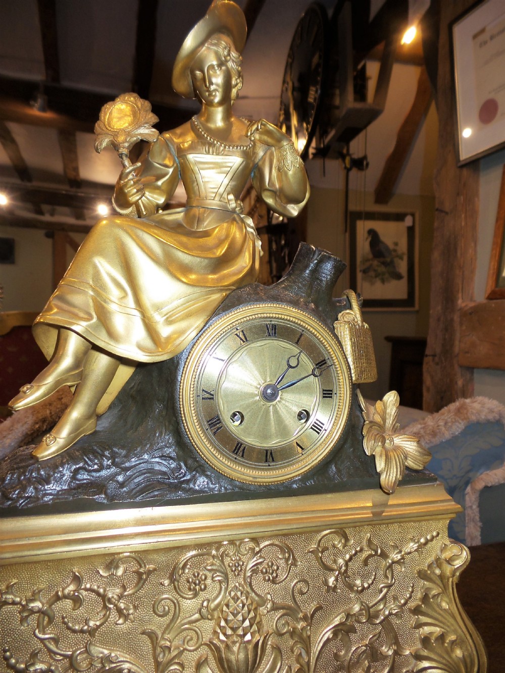 A mid-19th-century French gilt bronze and patinated bronze mantel clock featuring a seated female figure holding a fan atop an ornate sculpted base. View VI