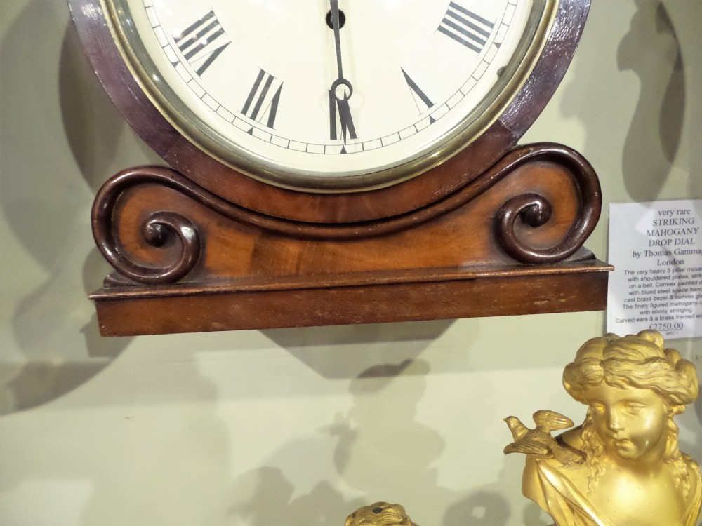 A 19th-century mahogany dial clock featuring a white circular face signed Ellis London with Roman numerals, a brass bezel, and carved scroll detailing at the base. View III