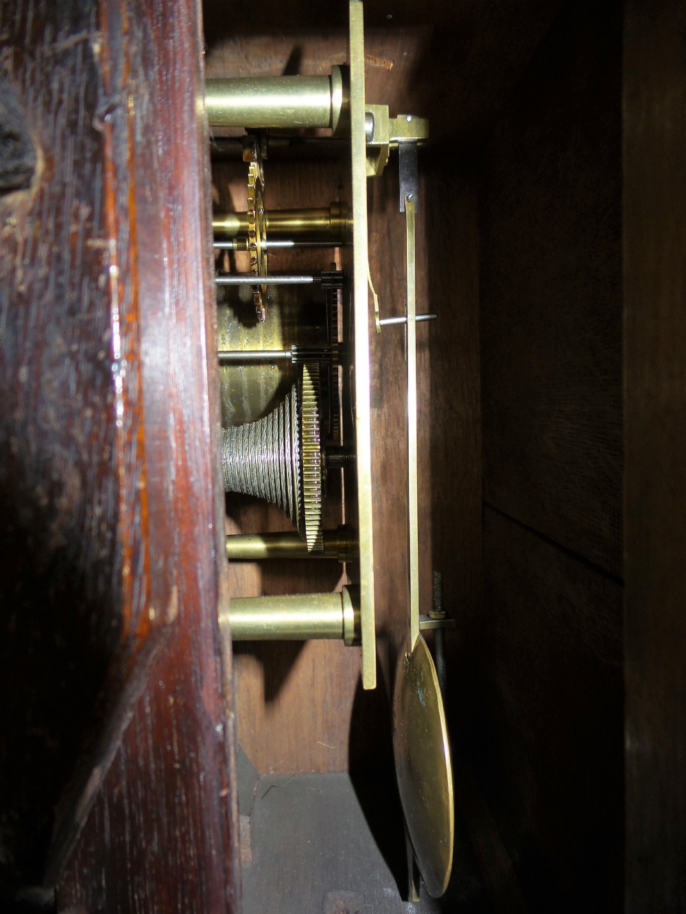 A 19th-century mahogany dial clock featuring a white circular face signed Ellis London with Roman numerals, a brass bezel, and carved scroll detailing at the base. View IV