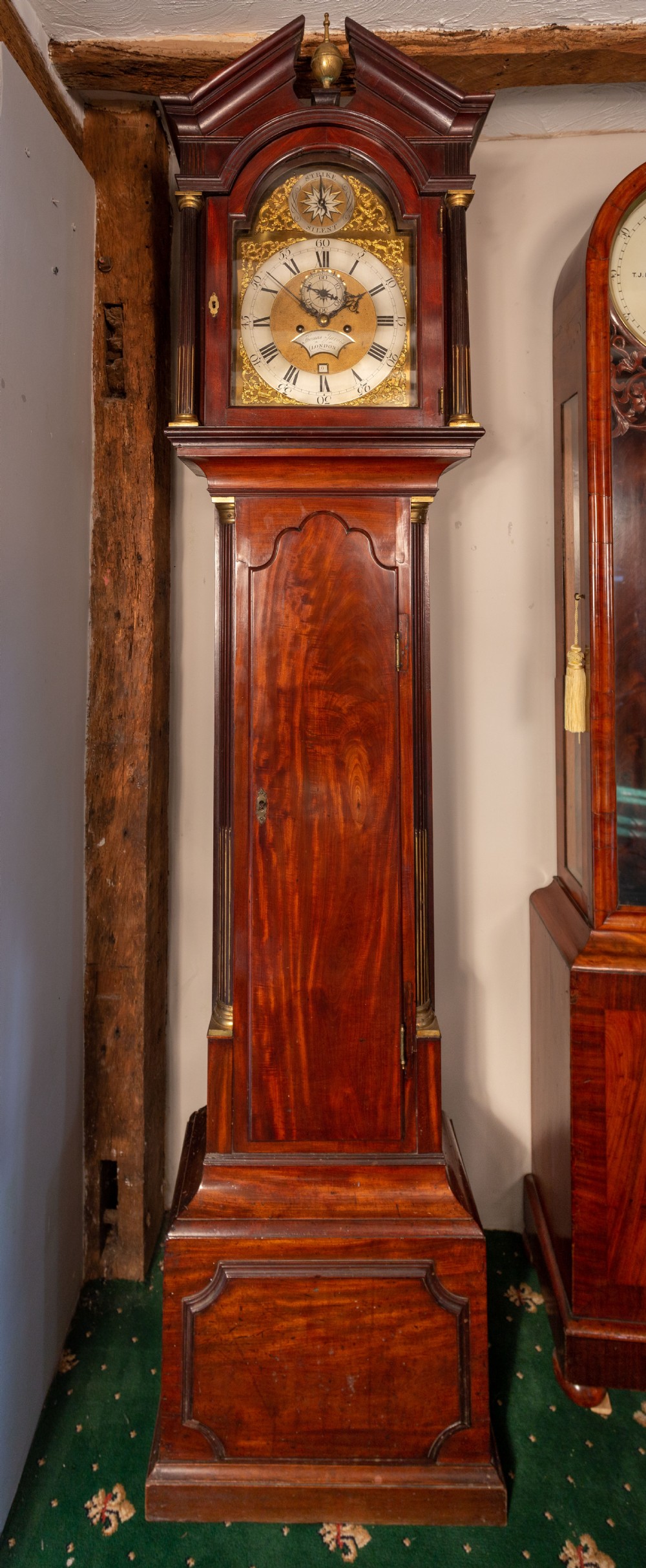 A Georgian flame mahogany eight-day longcase clock featuring a pedimented hood with fluted columns, a brass dial with spandrels, and a tall panelled case.