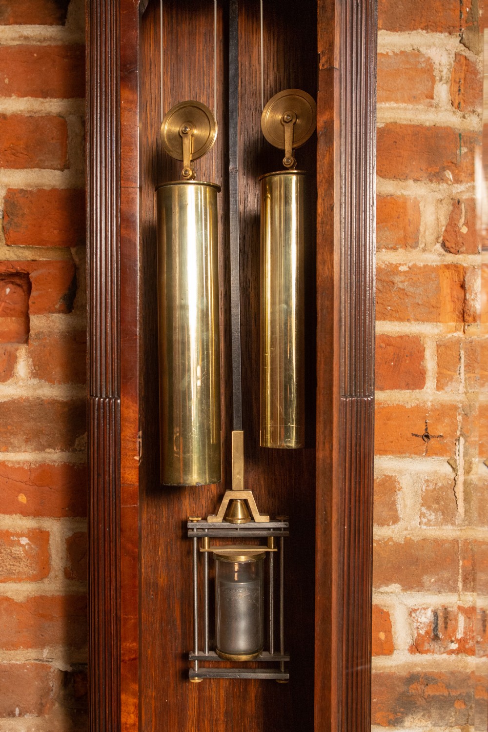 An Edwardian miniature mahogany longcase clock featuring a carved swan-neck pediment, brass moon phase dial, and glass trunk door revealing brass weights. View V