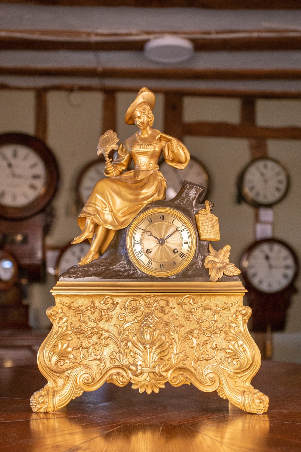 A mid-19th-century French gilt bronze and patinated bronze mantel clock featuring a seated female figure holding a fan atop an ornate sculpted base.