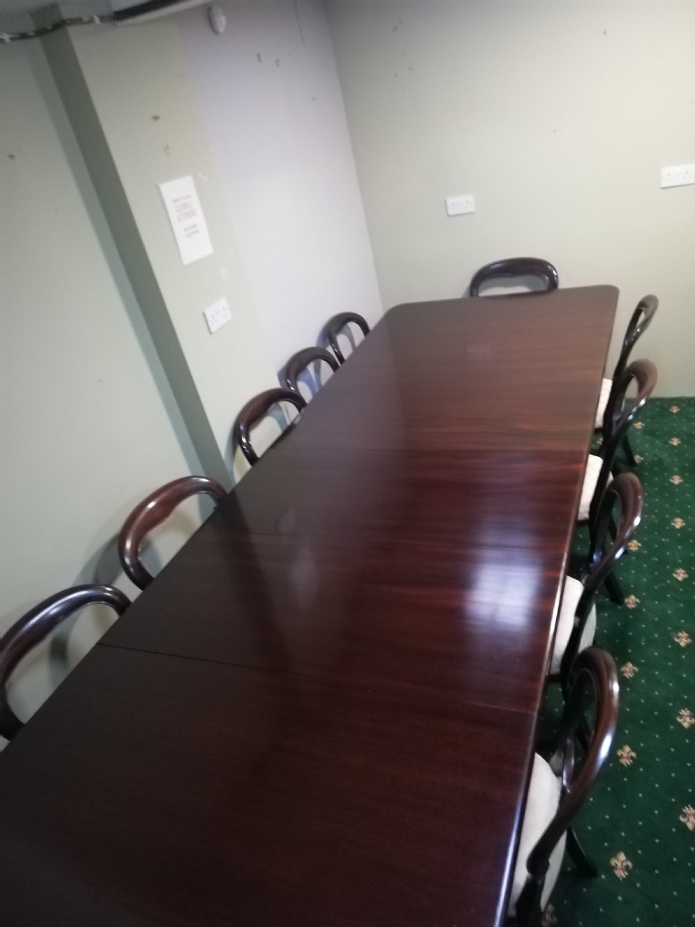 A long dark mahogany extending dining table surrounded by matching balloon back chairs with light fabric upholstered seats.