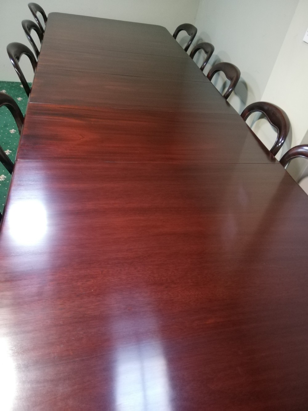A long dark mahogany extending dining table surrounded by matching balloon back chairs with light fabric upholstered seats. View X