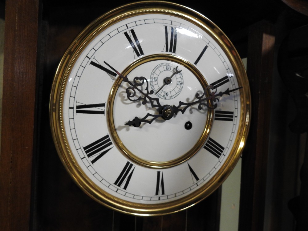 A nineteenth-century Vienna regulator wall clock featuring a shaped walnut glazed case, brass weights, pendulum, and a white enamel dial with Roman numerals. View V