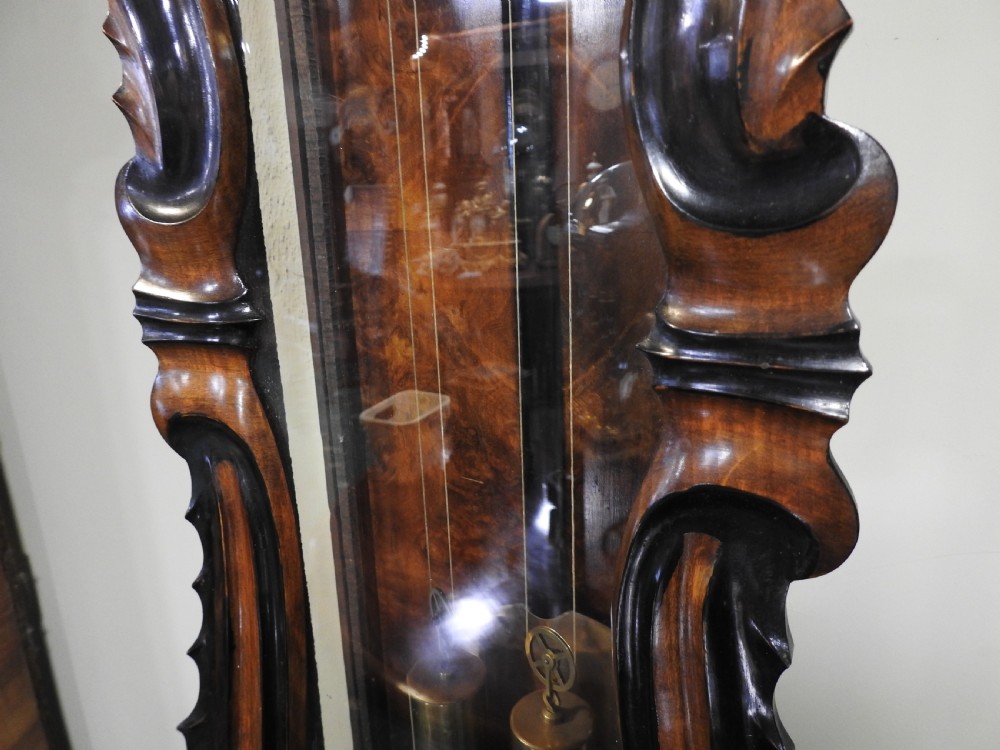 A nineteenth-century Vienna regulator wall clock featuring a shaped walnut glazed case, brass weights, pendulum, and a white enamel dial with Roman numerals. View VI