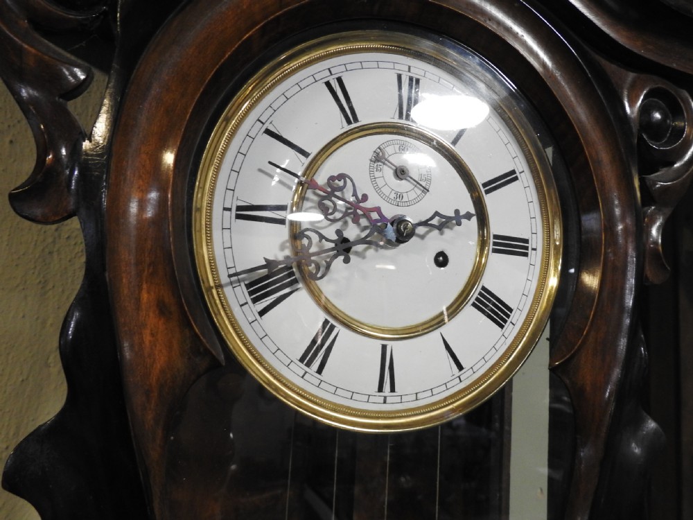 A nineteenth-century Vienna regulator wall clock featuring a shaped walnut glazed case, brass weights, pendulum, and a white enamel dial with Roman numerals. View X