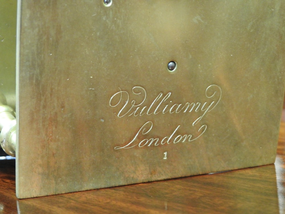 An antique Regency flame mahogany bracket clock featuring a gabled top, a silvered dial signed Vulliamy London, and brass ball feet. View IV